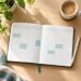 Agenda semanal abierta sobre un escritorio con un bolígrafo, una taza de café y una planta.