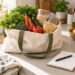 Bolsa reutilizable con alimentos junto a un cuaderno para la lista de compra.