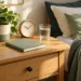 Reloj, cuaderno y vaso de agua junto a una cama en una habitación luminosa